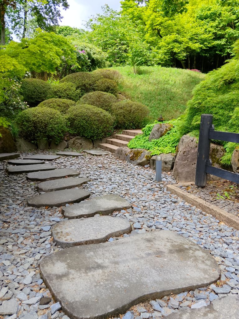 A peaceful stone pathway winds through a green and serene Japanese garden.